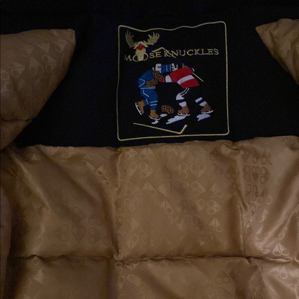 Moose Knuckles Black and Gold Jacket with the moose knuckle logo on the side arm